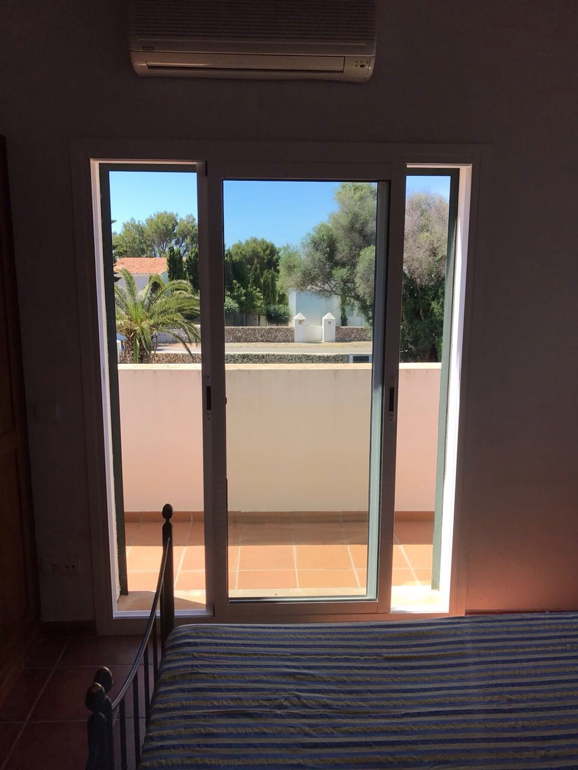 A room with a bed, a sliding glass door leading to a balcony, and an air conditioning unit above the door.