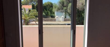 A room with a bed, a sliding glass door leading to a balcony, and an air conditioning unit above the door.