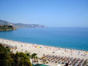 Ein Strand mit Sonnenschirmen und Liegestühlen, ein klarer Himmel und ruhiges Meer.