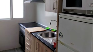 A compact kitchen with wooden cabinets, a microwave, a sink, and a window. - apt a5min apie from the beach (Málaga)