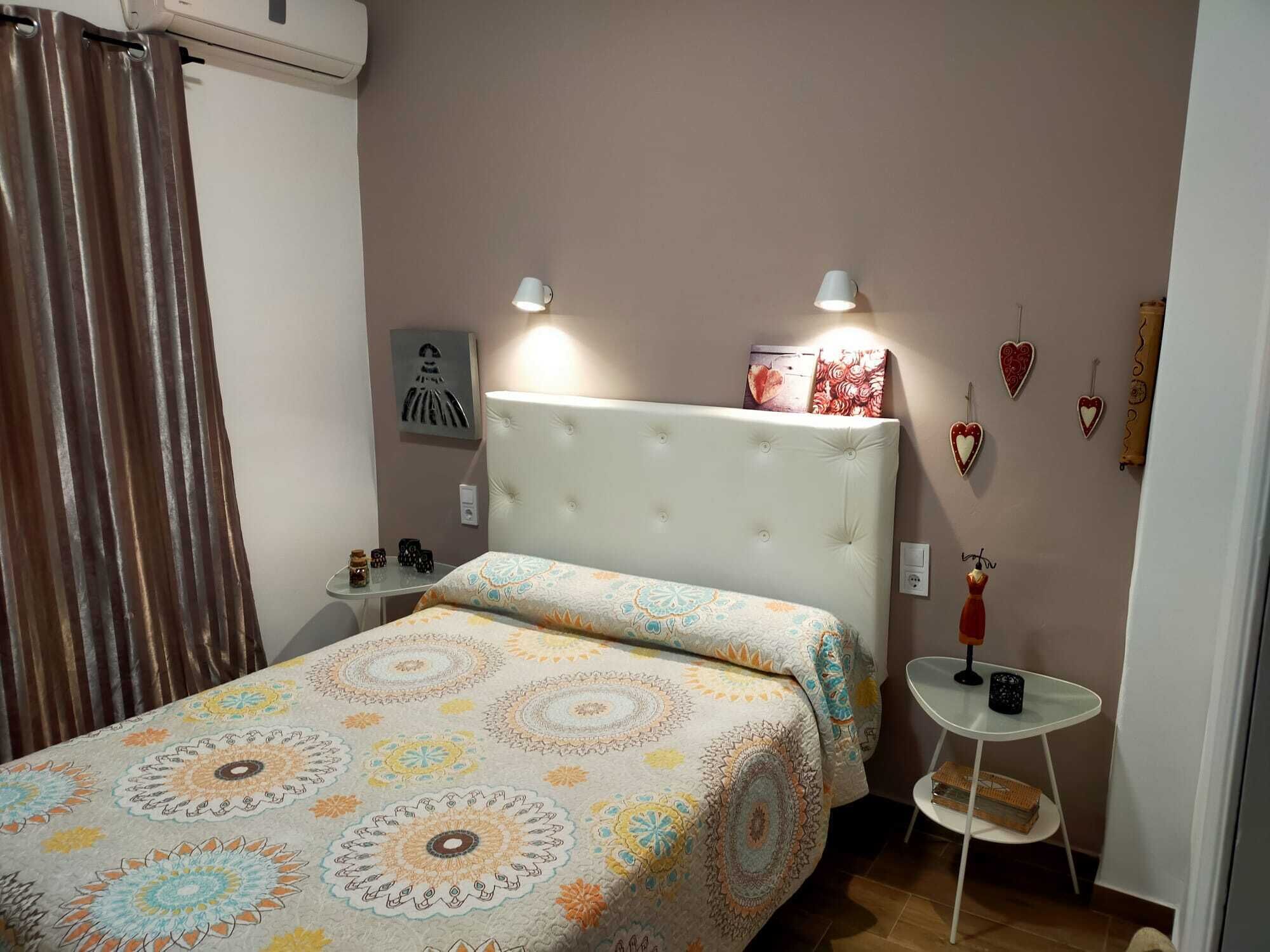 Une chambre à coucher avec un lit, deux lampes de chevet, une petite table et des objets décoratifs en forme de cœur accrochés au mur.