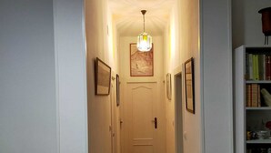 A narrow hallway with wooden flooring, white walls, and a chandelier. There are framed pictures on the walls and a bookshelf on the right. - apt a5min apie from the beach (Málaga)