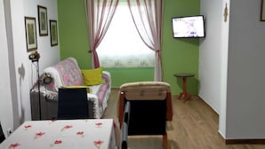 A room with a green wall, a bed with a floral bedspread, a TV on the wall, and a small table. - apt a5min apie from the beach (Málaga)
