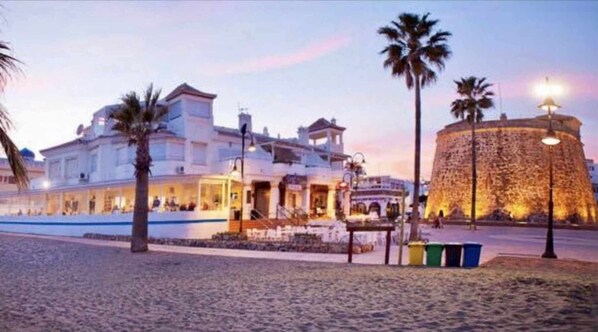 A coastal building with a stone tower, palm trees, and a beach in the foreground. - Mi Capricho 170 Beachfront Apartment (Mijas)