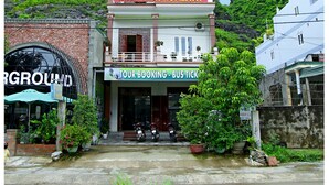 Edifício de dois andares chamado Hoan Chau Homestay com uma varanda, rodeado por vegetação exuberante e ao fundo, montanhas.
