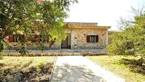 Un edificio in pietra con tetto in tegole, un vialetto in pietra che conduce all'ingresso e vegetazione circostante.