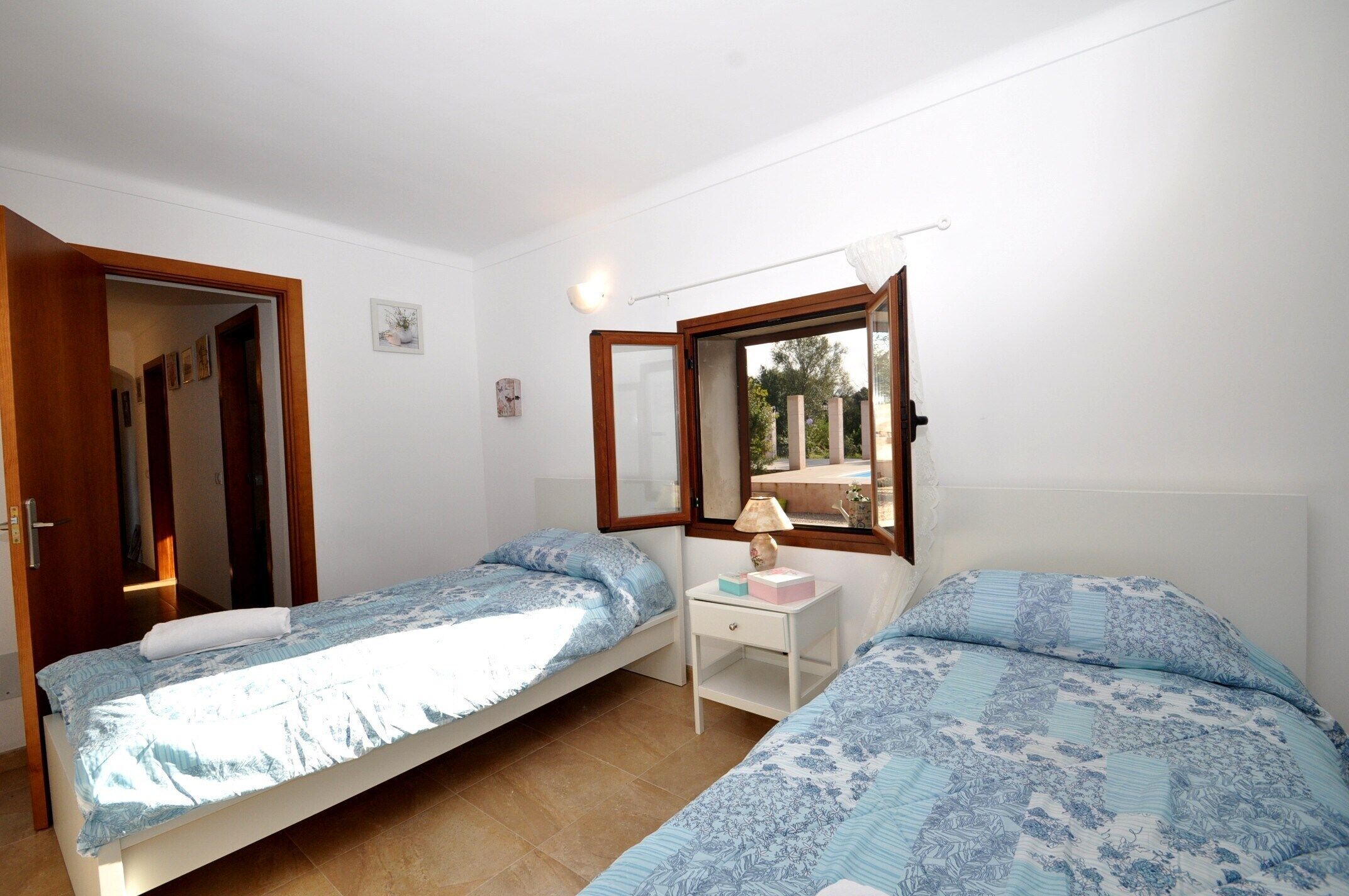 Quarto com duas camas de solteiro, mesa de cabeceira com abajur e janela com vista para o exterior.