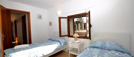 Quarto com duas camas de solteiro, mesa de cabeceira com abajur e janela com vista para o exterior.