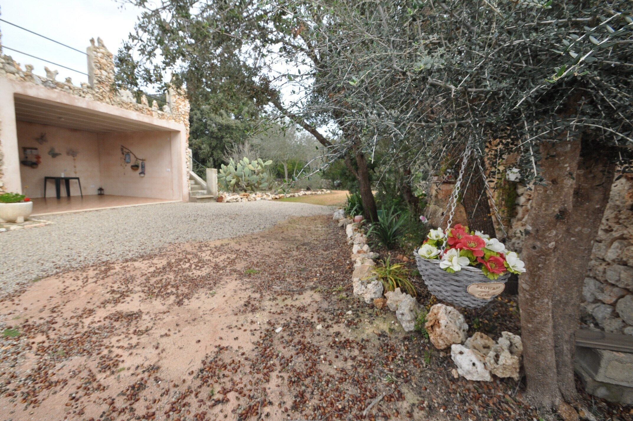 Un edificio rústico de piedra con una terraza abierta, un muro de piedra con una cesta de flores colgante y un camino de grava.
