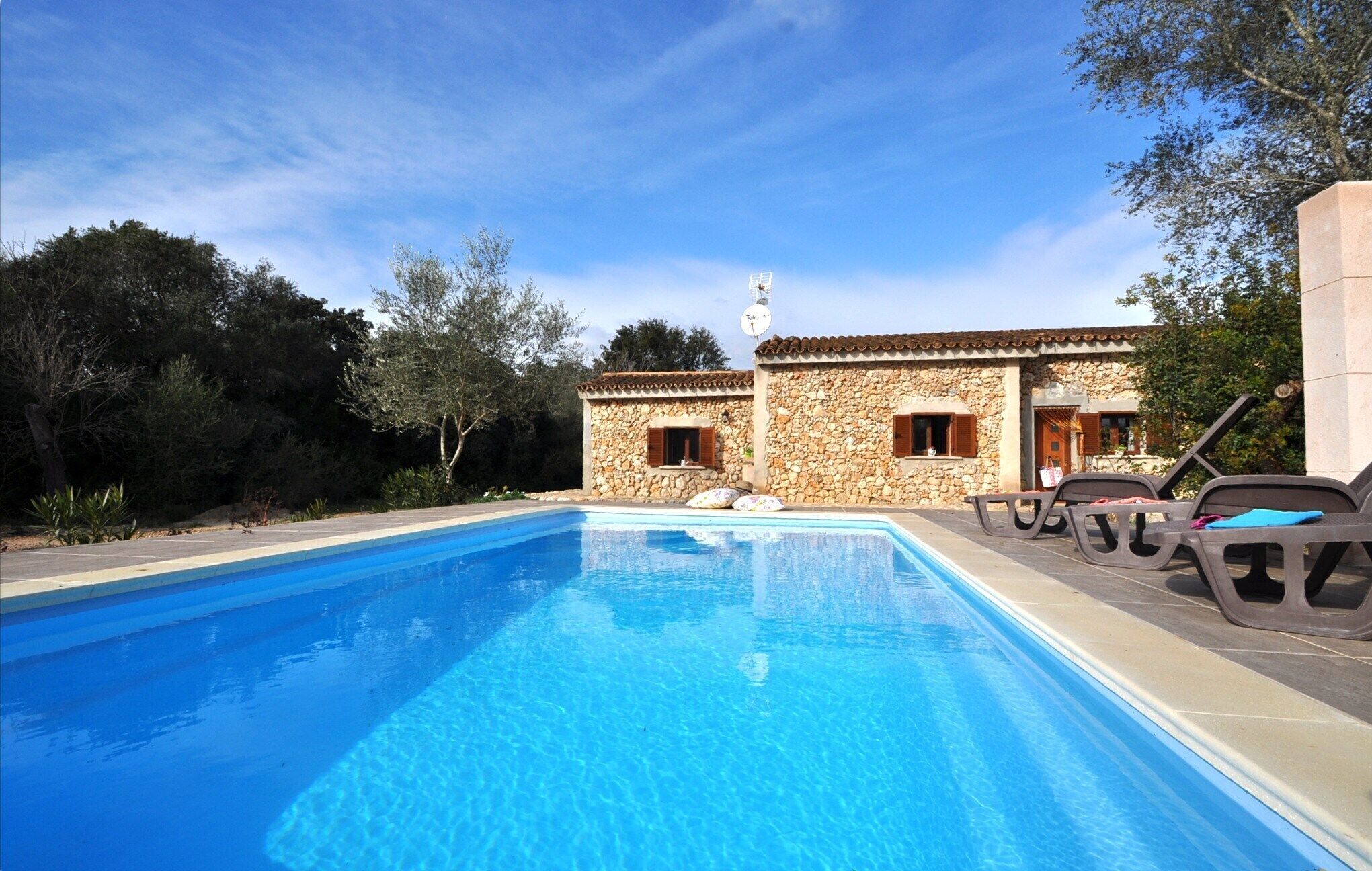 Un edificio de piedra con piscina y sillones de descanso.