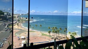 A view from a window overlooking a beach with palm trees, a road, and buildings in the distance.
