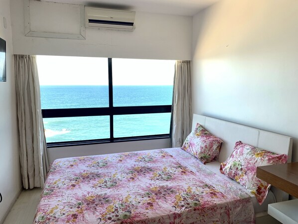 A bedroom with a bed, a nightstand, and a window with a view of the ocean.