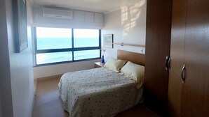 A bedroom with a bed, a wardrobe, a window with a view of the sea, and a ceiling light.