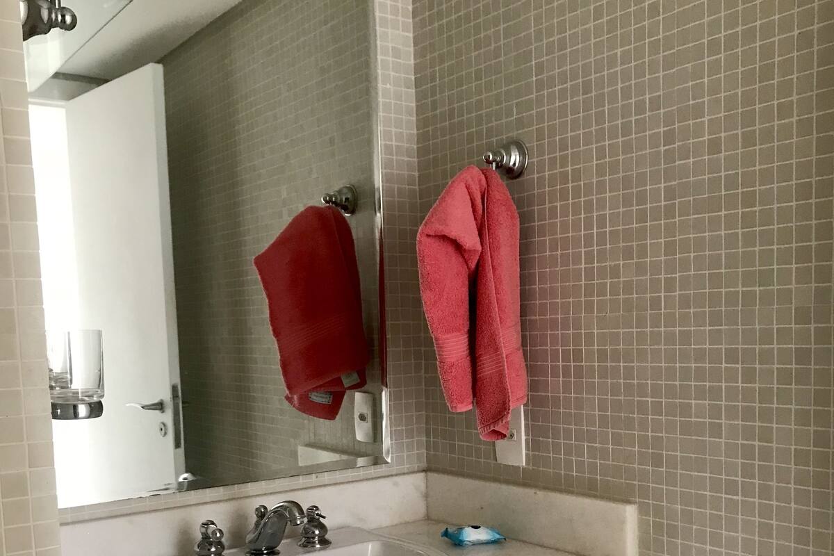 Une salle de bain avec un lavabo blanc, deux porte-serviettes avec des serviettes rouges, un miroir et des murs carrelés.