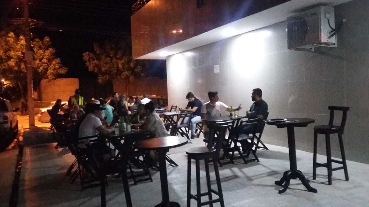 An outdoor seating area with tables and chairs, surrounded by a low wall and trees.