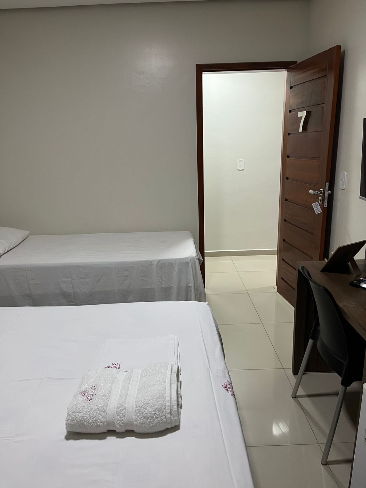 Une chambre d’hôtel avec deux lits, un bureau avec un ordinateur et une porte en bois portant le numéro 7.