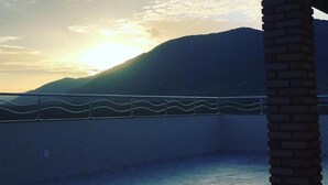 En balkon med udsigt til havet og et bjerg i solnedgangen.