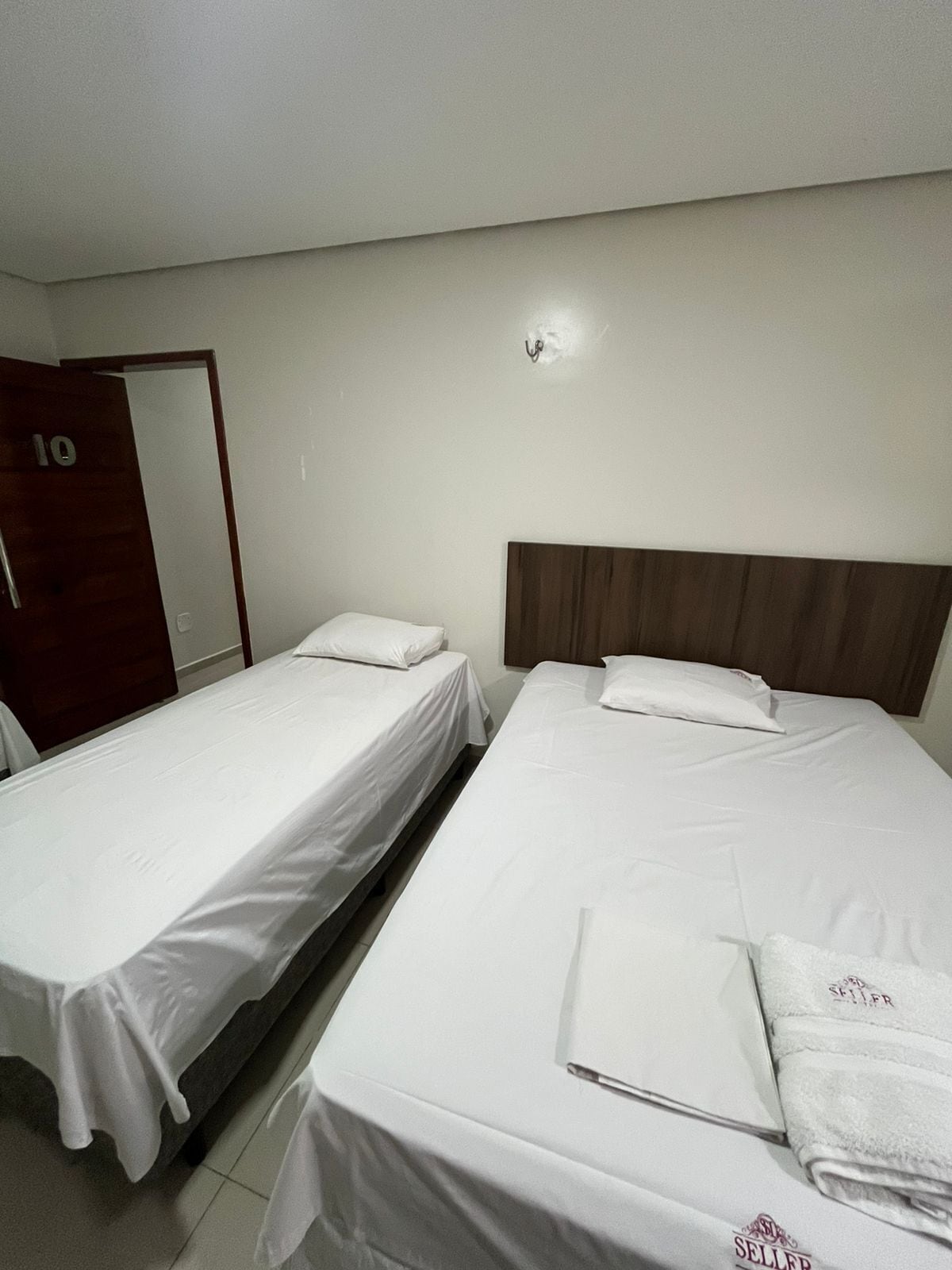 A hotel room with two single beds, a wooden wardrobe, and a door marked with the number 10.