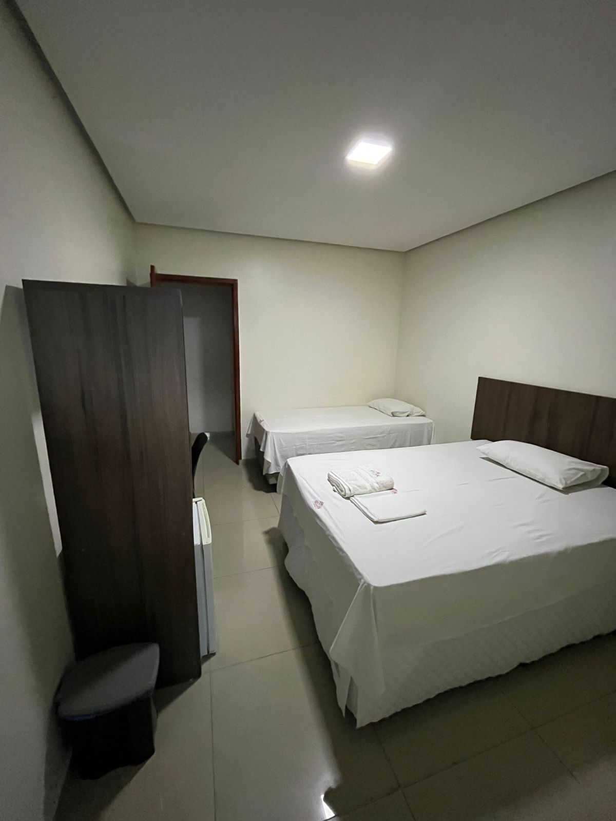 A hotel room with two beds, a desk, a chair, and a wardrobe.
