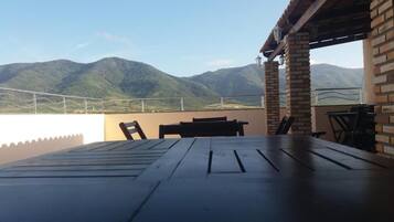 A terrace with a table and chairs, overlooking a mountainous landscape.