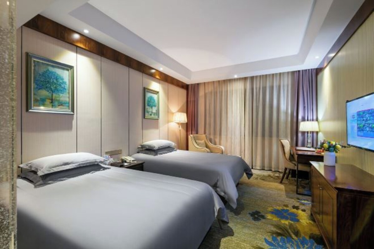 A hotel room with two beds, a desk, a chair, a TV, and a painting on the wall.