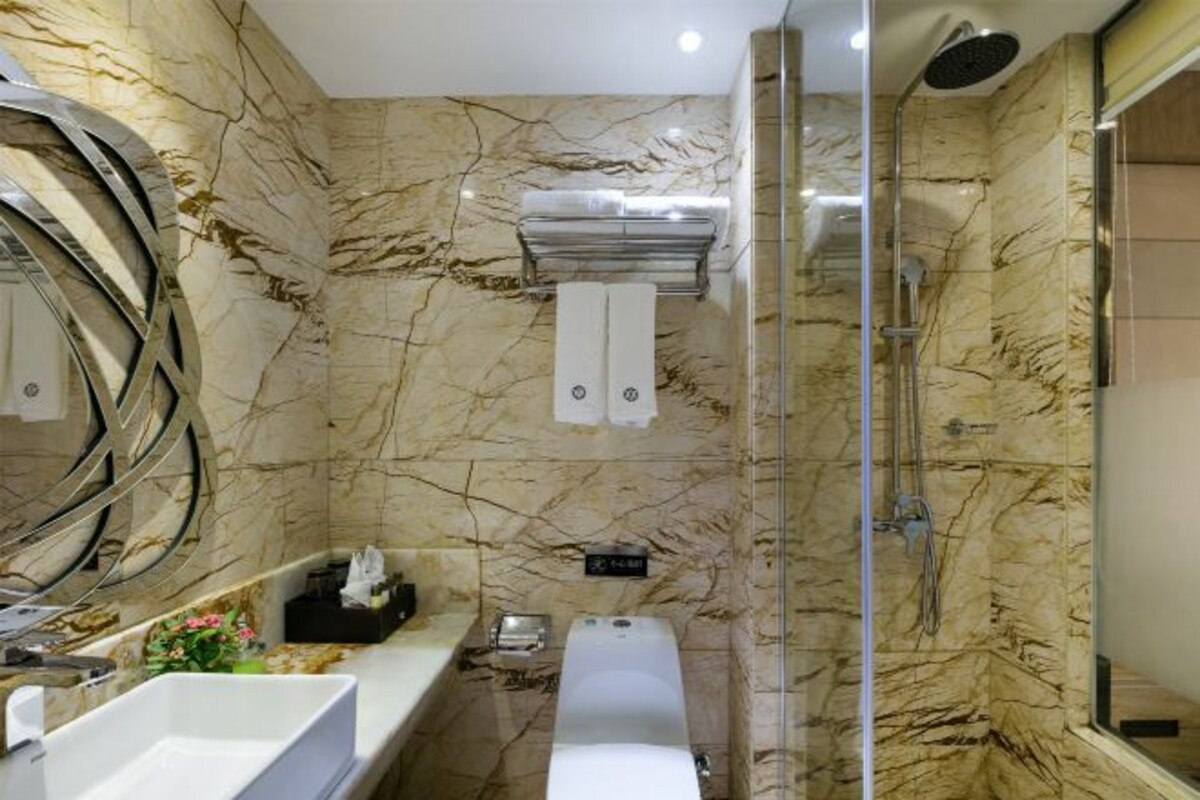 A modern bathroom with marble walls, a large mirror, a bathtub, and a shower.