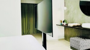 Un baño moderno con un espejo grande, un televisor de pantalla plana y un tocador con lavabo y espacio para toallas.