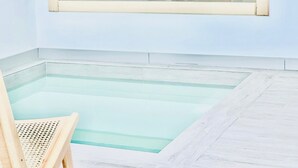 Una pequeña piscina interior con una silla de madera y un sillón de mimbre.