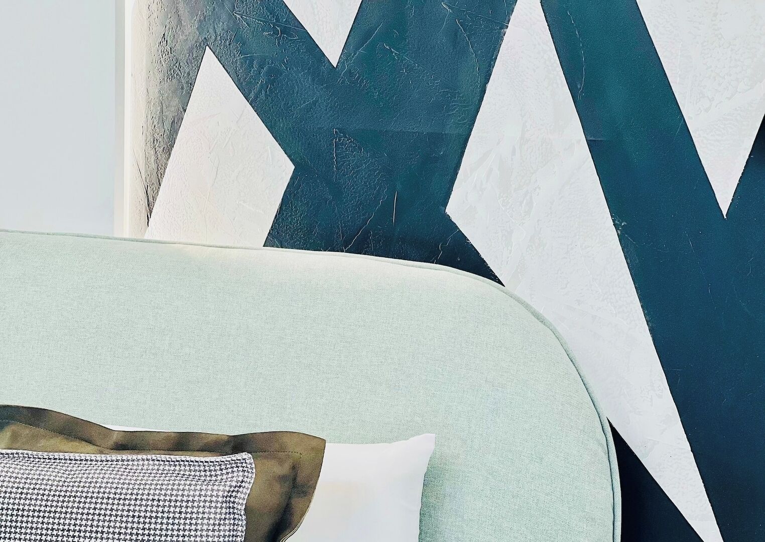 A room with a light green sofa and a large abstract painting with dark blue and white shapes.