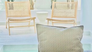 Una habitación con dos sillas de madera con respaldo trenzado, un cuenco blanco sobre una mesa y un cojín de cuadros sobre un sofá azul.