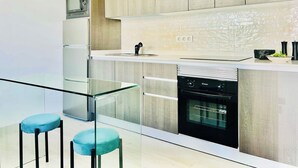 Cocina moderna con horno integrado, microondas y pileta. Hay dos taburetes azules y una baranda de vidrio.