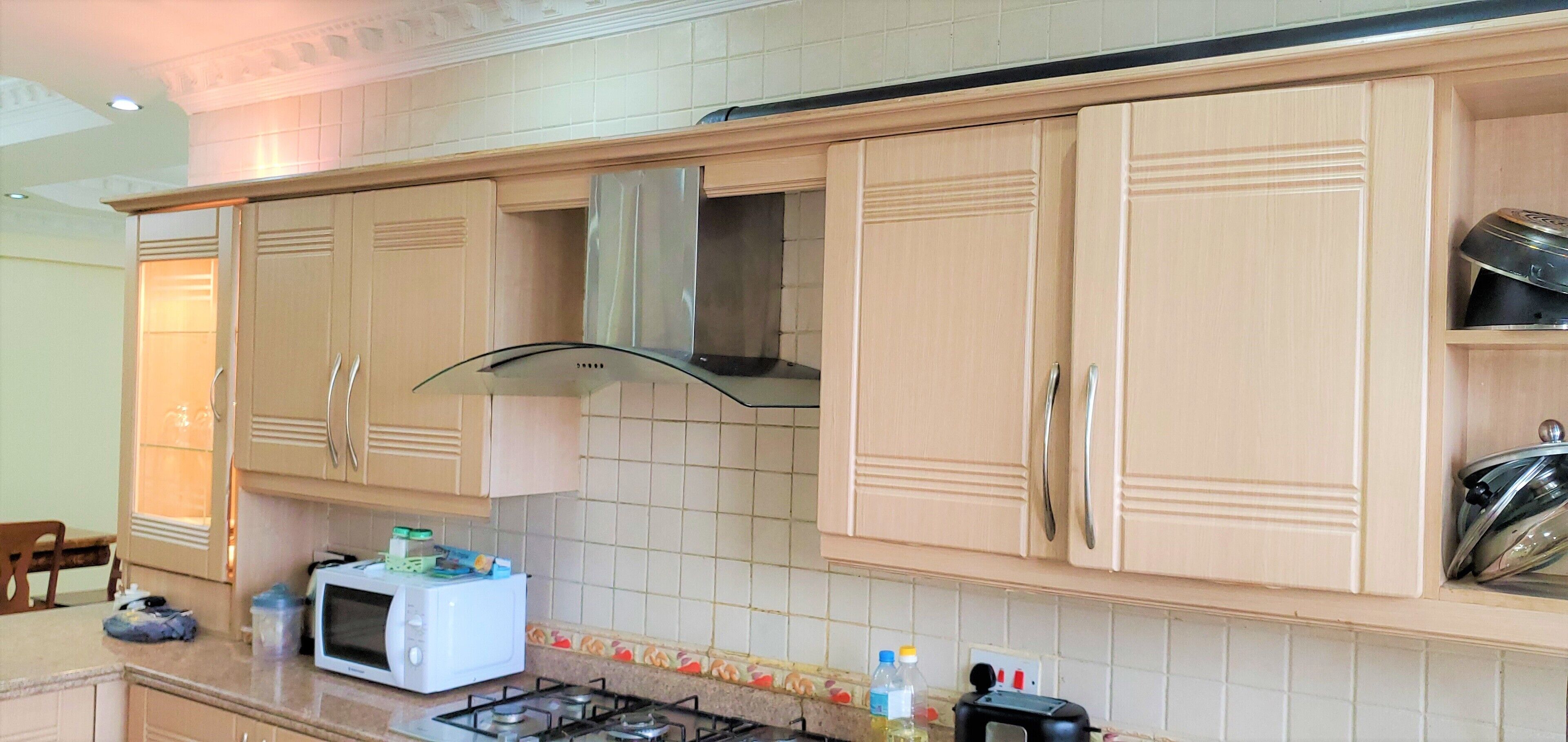 Una cocina con gabinetes color beige, una campana extractora de acero inoxidable, un microondas y una estufa a gas.