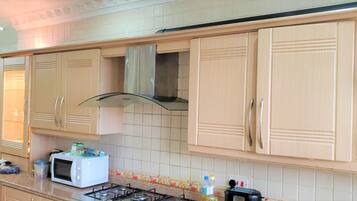 Una cocina con gabinetes color beige, una campana extractora de acero inoxidable, un microondas y una estufa a gas.