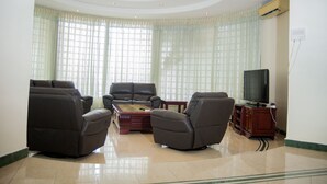 A spacious living room with a large window, a flat-screen TV, and a fireplace. - Luxury Residence with Ocean View in Masaki (Dar es Salaam)