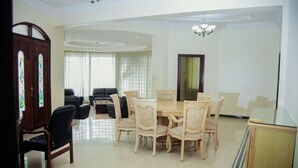 A dining area with a round table and six chairs, a wooden cabinet, and a large window with curtains. - Luxury Residence with Ocean View in Masaki (Dar es Salaam)