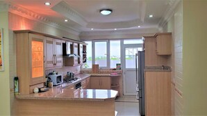 A modern kitchen with wooden cabinets, a central island, and a large window providing a view of the outdoors. - Luxury Residence with Ocean View in Masaki (Dar es Salaam)