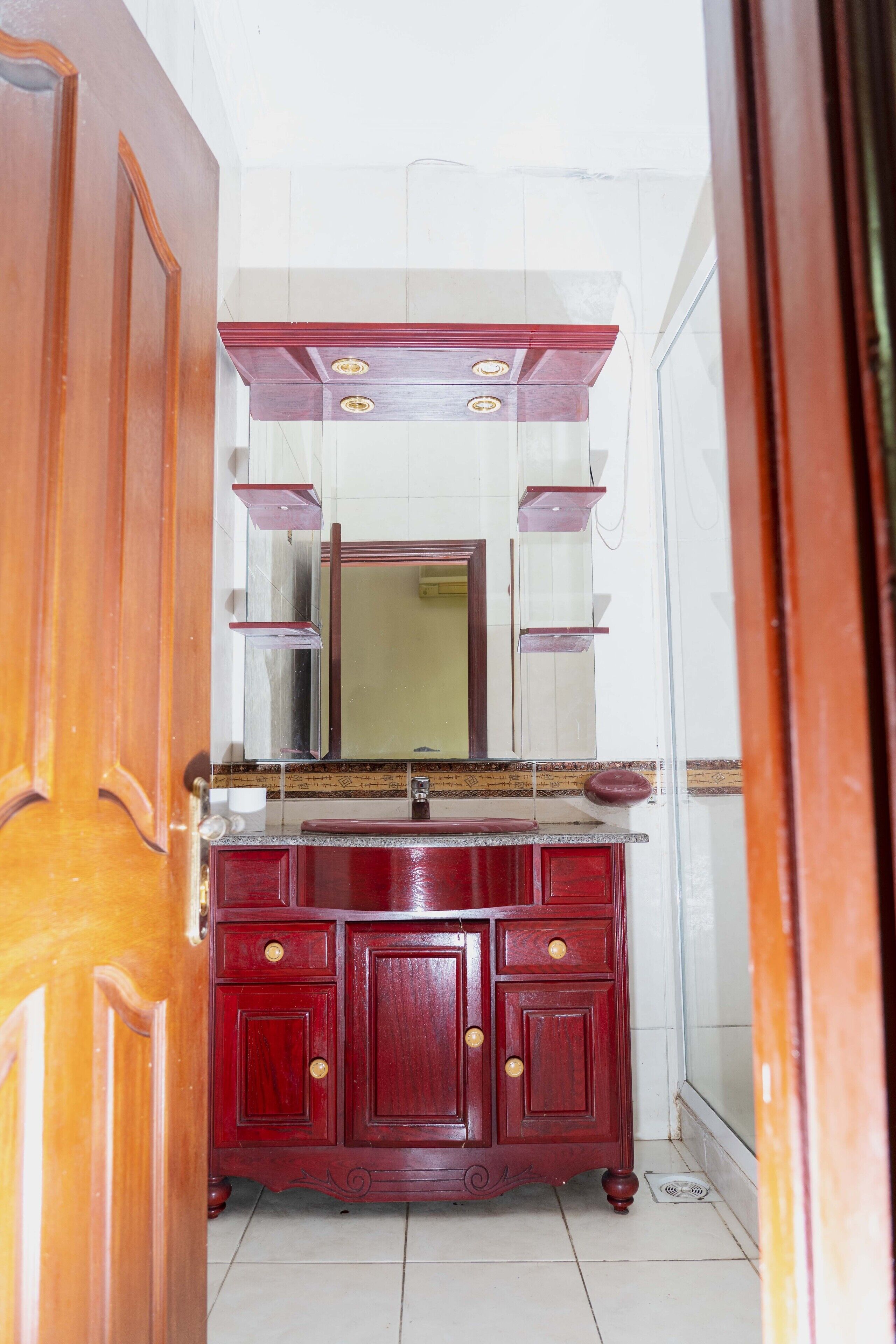 Een houten wastafelmeubel met spiegel en lades, in een kamer met witte wanden en een betegelde vloer.