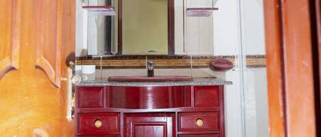 A wooden vanity with a mirror and drawers, located in a room with white walls and a tiled floor.