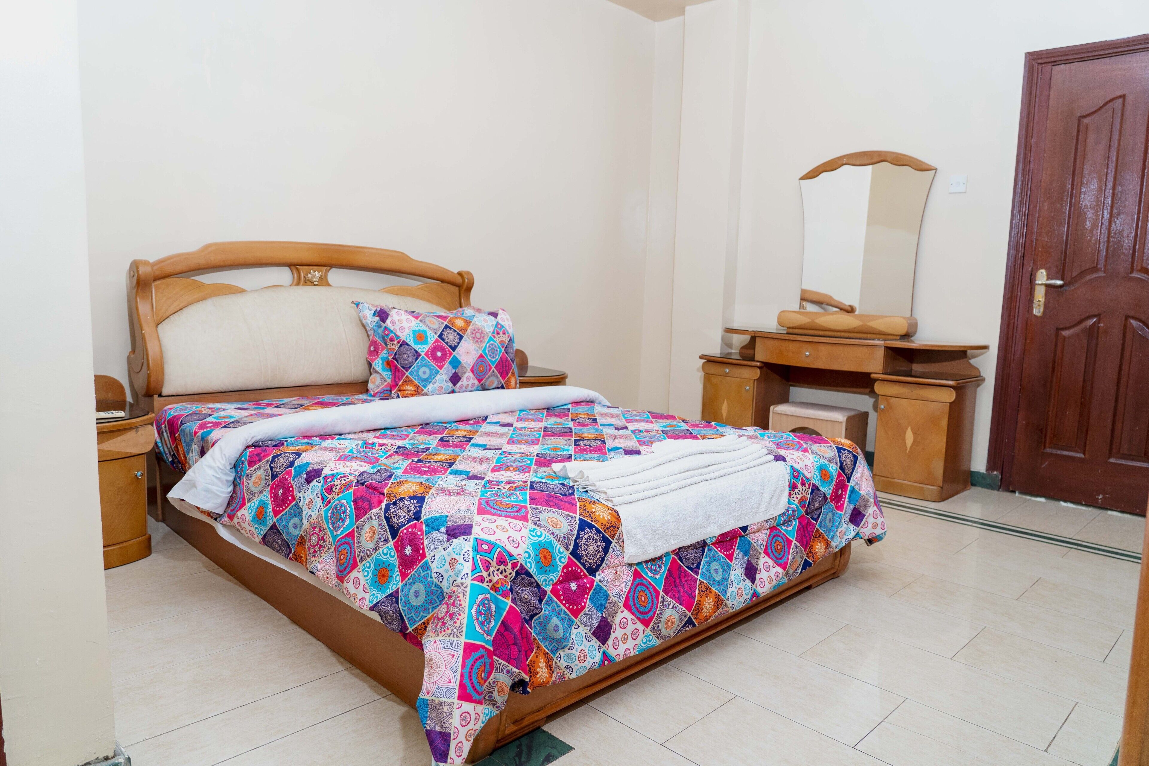 Un dormitorio con una cama de madera, una mesita de noche, un aparador, un espejo y una puerta.
