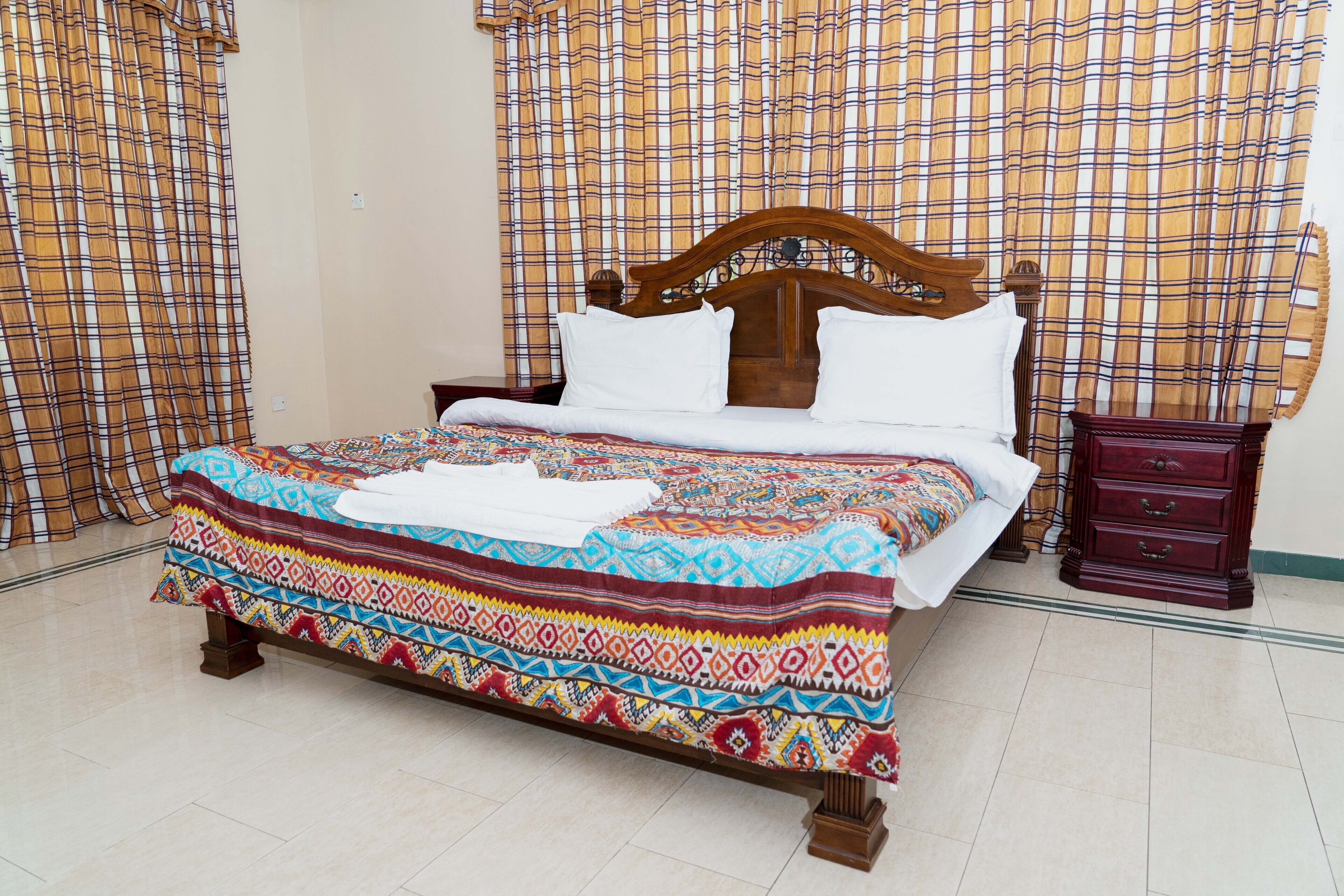 A bed with a colorful blanket and pillows, a wooden nightstand, and a dark wooden dresser.