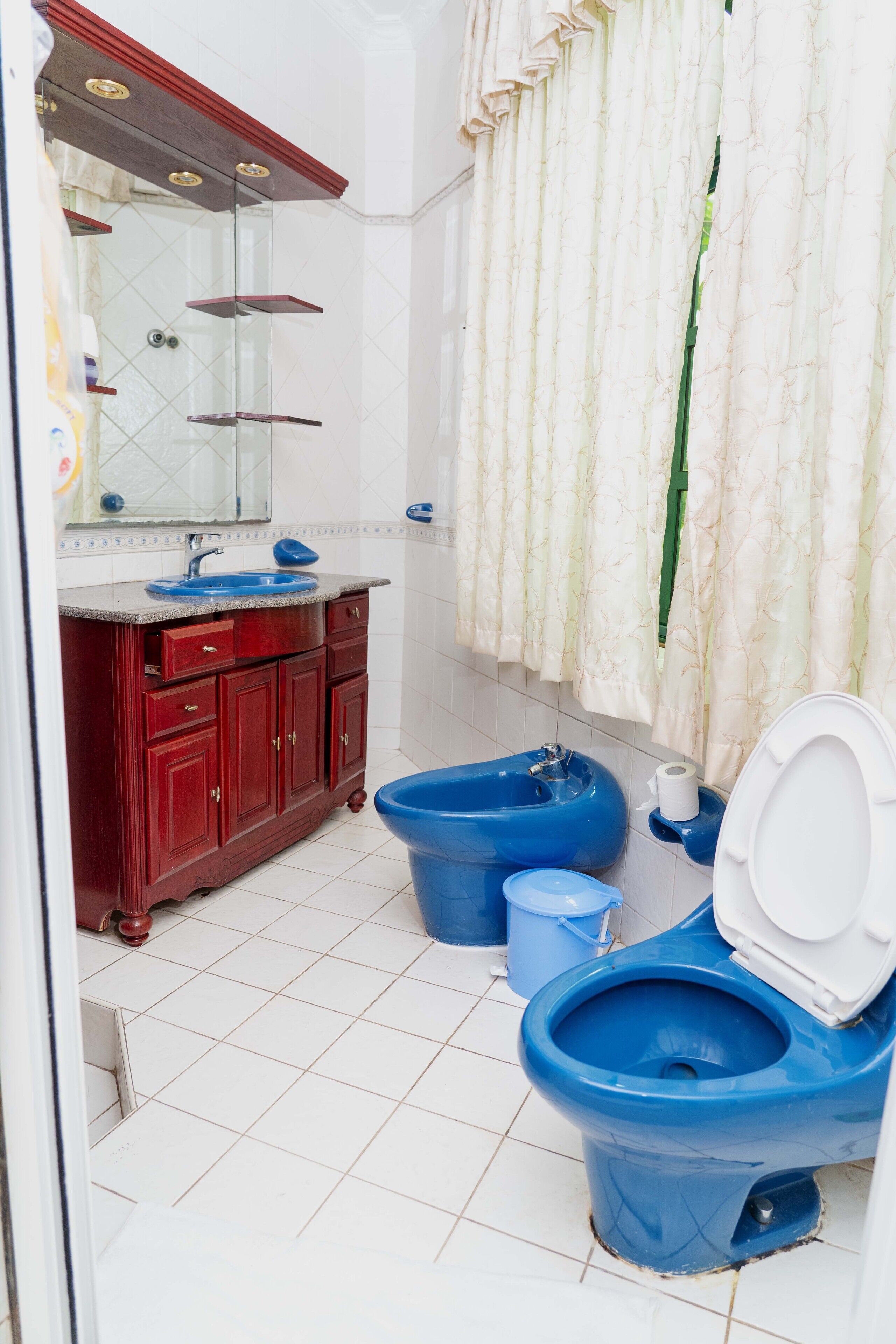 A bathroom with a red vanity, a blue sink, and two blue toilets.