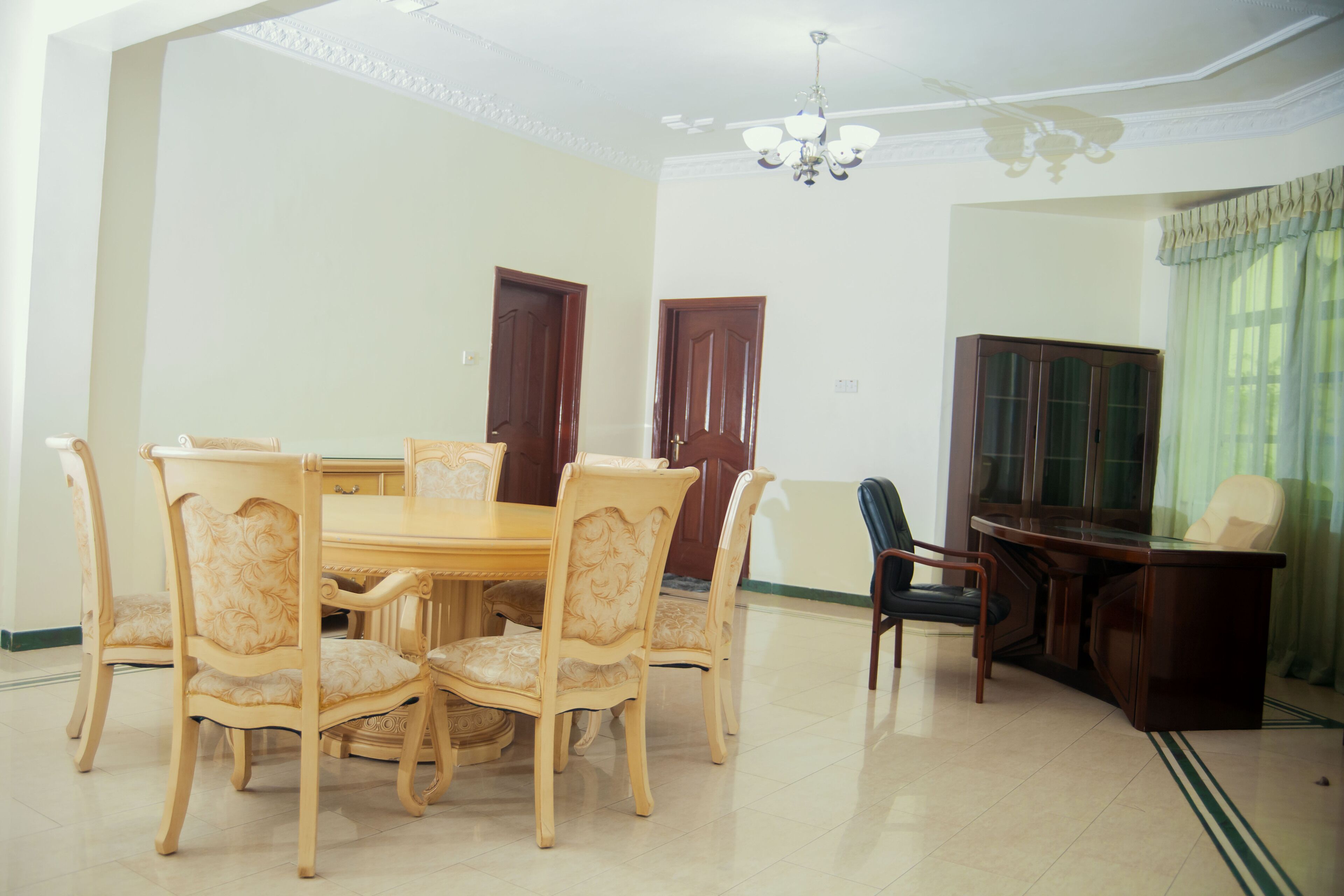 A dining area with a round table and six chairs, a wooden cabinet, and a desk with a chair.