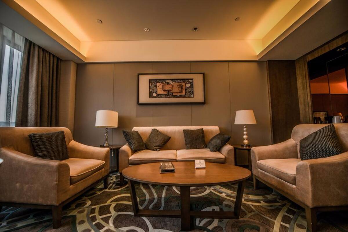 A hotel room with a sofa set, two side tables with lamps, a framed artwork on the wall, and a patterned carpet.