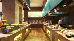 A buffet setup with multiple food stations and a chef preparing food in the background. - Maya Gleetour Hotel Wuhan (Wuhan)