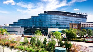 A modern building with a curved glass facade, surrounded by landscaped gardens and a parking area. - Maya Gleetour Hotel Wuhan (Wuhan)