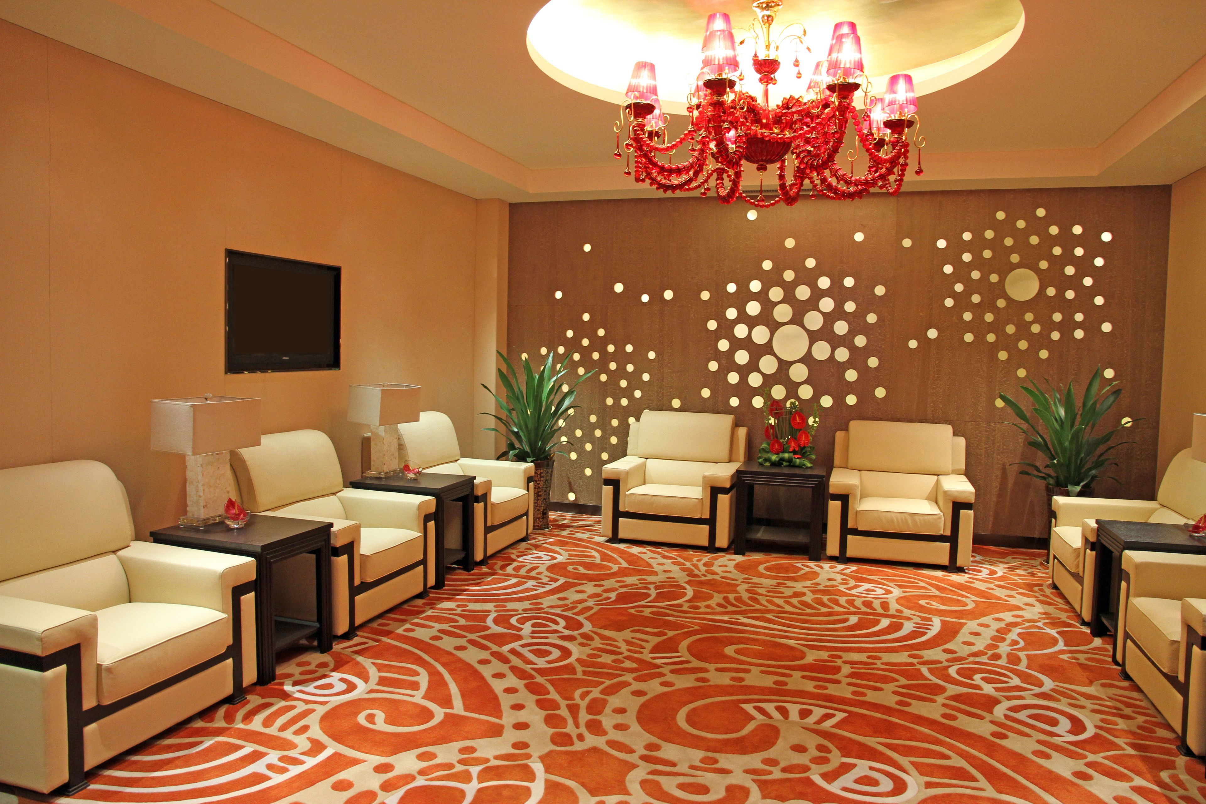 A hotel room with a patterned carpet, a chandelier, and multiple seating areas.
