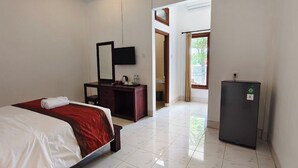 A hotel room with a bed, a desk, a mirror, a refrigerator, and a view of the outdoors. - Kusuma Homestay Kerobokan (Kerobokan)