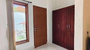 A room with a large window, a wooden door, and a wardrobe. - Kusuma Homestay Kerobokan (Kerobokan)