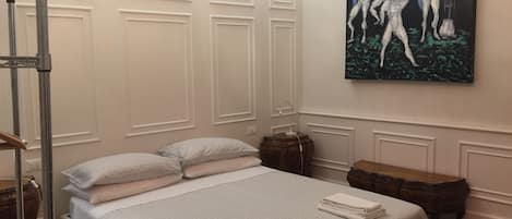 A neatly made bed with pillows, a painting on the wall, and a red chandelier.