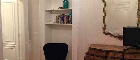 A room with a bed, a blue armchair, a wooden dresser, a bookshelf, and a mirror.
